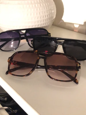 Tom Ford solglasögon fyrkantig brun - Snygga fyrkantiga solglasögon från Tom Ford med brunmelerad båge och bruna glas. Klassisk och trendig design med tydlig logga på linsen. Perfekta för dig som vill ha en exklusiv accessoar med statement-känsla.