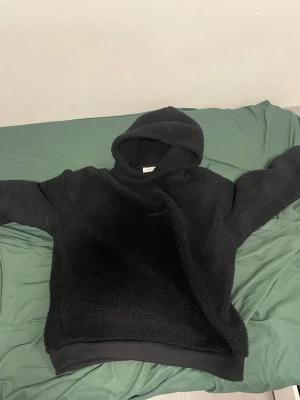 Svart teddyhoodie från Jack & Jones - Mysig svart hoodie från Jack & Jones i teddyfleece. Hoodien har en stor huva och ribbade muddar vid ärmslut och nederkant. Perfekt för dig som gillar en avslappnad och trendig stil. Materialet är fluffigt och ger en riktigt skön känsla.