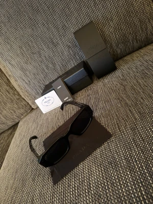 Svarta solglasögon från Prada - Snygga svarta solglasögon från Prada med rektangulär form och breda skalmar. Klassisk logga på sidan och stilren design. 