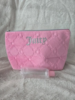 Rosa necessär från Juicy Couture - Söt rosa necessär från Juicy Couture i mjukt frottéliknande material med silverfärgad dragkedja och broderad Juicy-logga framtill. Väskan har ett quiltat mönster och är perfekt för smink eller småprylar. Enkel att ta med i väskan eller på resan.