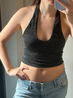 Svart glittrig halterneck topp - Snygg svart glittrig halterneck topp med djup urringning och öppen rygg. Stretchigt material som sitter tight. Perfekt till fest🪩🪩🪩använd en gång!