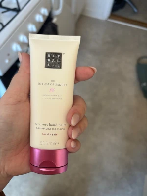 Rituals Sakura handbalsam - Rituals The Ritual of Sakura recovery hand balm är en återfuktande handkräm för torr hud. Tuben är ljusbeige med rosa metallic lock och rymmer 70 ml. Perfekt för dig som vill ha mjuka och välvårdade händer.