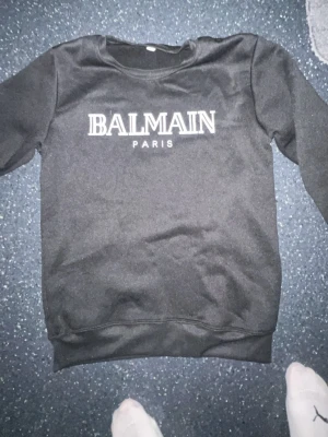 Svart sweatshirt från Balmain Paris - Cool svart sweatshirt från Balmain Paris med vit logotyp på bröstet. Tröjan har rund halsringning och ribbade muddar vid ärmslut och nederkant. Perfekt för dig som gillar exklusiva märken och enkel stil. Pris kan diskuteras 