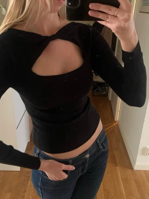 Svart topp med cut-out - Trendig svart croppad topp med lång ärm och snygg cut-out detalj över bröstet. Toppen har en tight passform och är ribbad.