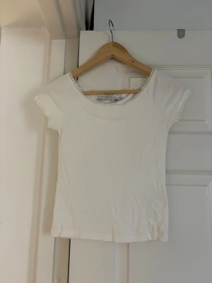 Vit spetskantad topp - Söt vit topp med korta ärmar och fina spetsdetaljer vid halsringning och ärmslut.