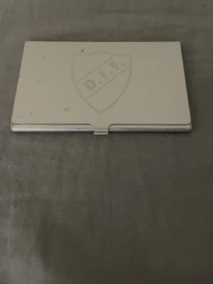 Silverfärgad plånbok med DIF-logga - Plånbok i silverfärgad metall med DIF-logga ingraverad på framsidan. Stilren och kompakt design som passar perfekt för kort och kontanter. Praktisk och enkel att ta med sig i fickan. Lite smutsig men går nog bort 