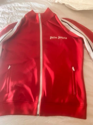Röd Palm Angels zip-tröja - Säljer min Palm Angels röd zip-tröja med vita detaljer och logga på bröstet. Den är värd 5000 men säljer den för 2500. Kan gå ner i pris om någon är intresserad! ❤️den är köpt i London och är i väldigt bra skick! Och den har inga defekter ☺️