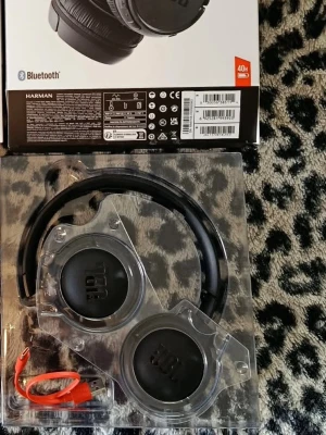 JBL trådlösa svarta hörlurar - Säljer ett par svarta trådlösa over-ear hörlurar från JBL med Bluetooth och lång batteritid. Hörlurarna har en stilren design med mjuka öronkuddar och justerbar båge. Medföljer laddningskabel och originalförpackning.