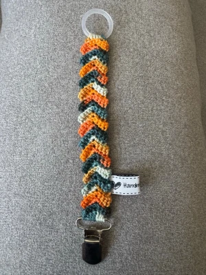 Virkad napphållare - Virkad, flerfärgad napphållar i blå och orangea toner.  Virkad av mig i 100% bomullsgarn med metallclip och silikonring.  Mönsterskapare: animo.design