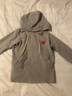 Grå hoodie från Comme des Garçons Play - Säljer en grå hoodie från Comme des Garçons Play. CDG är små i storlek så passar bättre XS. Riktigt snygg och passar till det mesta, har använt den en del men den är i bra skick utan några defekter! Vid frågor är det bara att skriva privat. Fraktas inom 24h!🤩