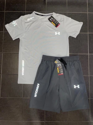 Under Armour träningsset t-shirt & shorts - Snyggt och sportigt set från Under Armour med t-shirt och matchande shorts. Perfekt för gym, träning eller vardag.  Båda plaggen är helt nya med tags, aldrig använda. Lätt och bekvämt material med reflexdetaljer – perfekt för både träning och stil.  ✔️ Skick: Helt nya (med tags) ✔️ Set: T-shirt + shorts ✔️ Passform: Sportig och bekväm M/S ✔️ Perfekt för gym, löpning eller vardag och perfekt för sommaren!  Riktigt clean set 🔥