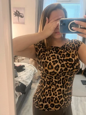 Leopardmönstrad topp från lager 157 - Snygg topp från 157 The Black Label Collection med leopardmönster i beige, brunt och svart. Klänningen har en rak passform och är ärmlös, perfekt för dig som vill sticka ut med ett djurmönster. Materialet känns mjukt och följsamt mot kroppen. Ändast använd en gång. 