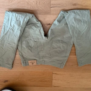 Ljusgröna jeans från Moreis - Säljer ett par ljusgröna jeans från Morris med raka ben och klassisk femficksmodell. Jeansen har synliga knappar i gylfen och patch med logga bak i midjan. Tillverkade i ett mjukt bomullstyg som ger en avslappnad look.