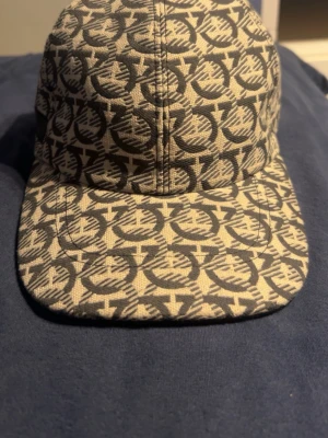 Beige keps med svart mönster - Snygg keps i beige med svart grafiskt mönster över hela ytan. Klassisk böjd skärm och justerbar rem baktill. Tillverkad i ett slitstarkt tygmaterial som ger en cool och trendig look.