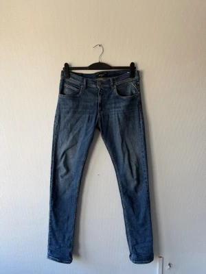 Replay  - Säljer ett par blå slim fit jeans från Replay med klassisk femficksdesign och snygga detaljer. Jeansen har en normal midja och raka ben, tillverkade i bomull med stretch för extra komfort. Perfekt för dig som gillar en tidlös och avslappnad look.