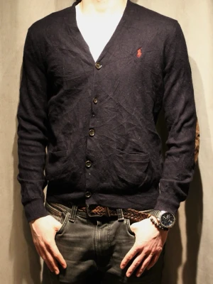 Mörkblå cardigan från Polo Ralph Lauren - Mörkblå cardigan med knappar och två fickor framtill från Polo Ralph Lauren. Klassisk design med röd broderad logotyp på bröstet och v-ringad hals. Materialet är mjukt och tunt, perfekt för lager-på-lager. Snygg och enkel att matcha.