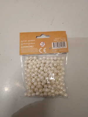 Paket med vita pärlor - Ett paket med vita runda pärlor i plast, perfekta för att skapa egna smycken som armband, halsband eller andra accessoarer. Pärlorna har hål för att enkelt kunna träs på tråd eller wire. Passar dig som gillar att pyssla och designa unika smycken.