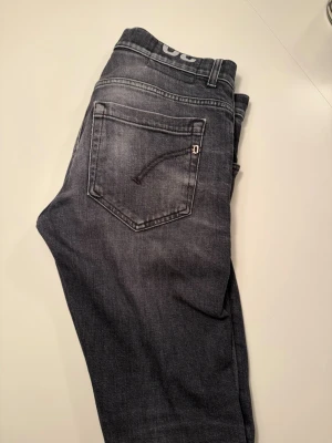 Svarta dondups med tvätt stil  - Snygga mörkgrå jeans med tvättad effekt och raka ben. Bakfickorna har diskreta sömmar och en liten metall-detalj. Klassisk femficksmodell i mjukt denimtyg, perfekta till vardagsstilen.