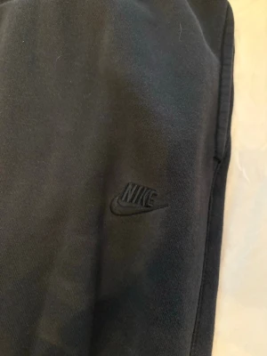 Svarta Nike dress  - Svarta mjukisbyxor från Nike med broderad logga på benet. Byxorna har resår i midjan med dragsko och är gjorda i mjukt, fleeceliknande material på insidan. Perfekta för chill eller träning. Hoodie där dragkedjan har gått sönder. Hoodie är M och byxorna är L