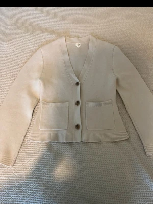 Arket kofta i bomull - Snygg beige kofta med v-ringning och tre knappar framtill. Koftan har två stora fickor på framsidan och ribbade muddar vid ärmslut och nederkant. Perfekt att slänga över en t-shirt för en chill look. Har använts en gång så är som en ny.