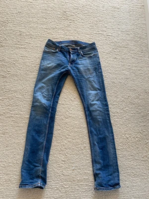 Nudie Jeans Grim Tim - Säljer ett par Nudie Jeans i modellen grim tim. Dessa jeans har använts en del men har tagits väl hand om. Slitningarna (se bilder) är där det har lagats, jag har alltså lämnat in dessa till Nudies butik för lagning 1 gång. 