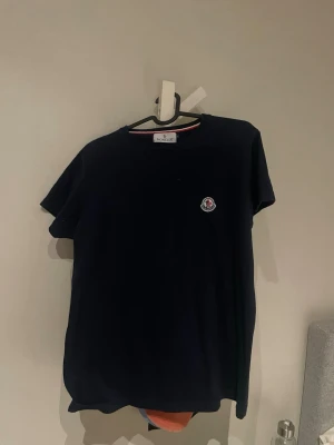 Mörkblå Moncler t-shirt  - Snygg mörkblå t-shirt från Moncler med klassisk rund hals och Moncler-logga på bröstet. T-shirten har en enkel och stilren design med korta ärmar och är tillverkad i mjuk bomull för skön komfort.