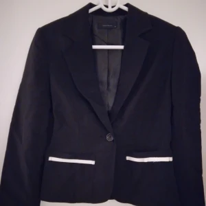 Kort svart kavaj från Vero Moda. Strlk: 34 / XS. Felfri.  - Kort svart kavaj från Vero Moda med 2 fickor.  Strlk: 34 / XS. Material: Polyester + satinfoder. Stängs med knapp. Endast använd 1 gång. Felfri.  Modellen visar liknande kavaj och passform.