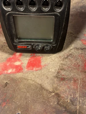 Koso - Säljer en svart digital instrumentpanel från Koso med stor display och flera knappar upptill. Panelen har två tryckknappar nedtill och är tillverkad i plast. Perfekt för dig som vill uppgradera eller byta ut din nuvarande instrumentpanel