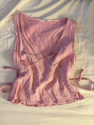 Rosa omlottopp med broderade blommor - Säljer denna supersöta toppen från stradivarius, den har två band för en figurnära form ochär i mycket bra skick då den endast är testad!