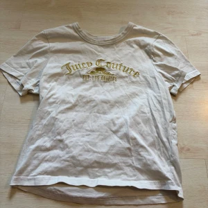 Vit Juicy Couture t-shirt - Juicy Couture t-shirt i vit bomull med guldfärgad logga och text 'EST. LOS ANGELES' på bröstet. Klassisk rund hals och korta ärmar, perfekt för en avslappnad och cool look.