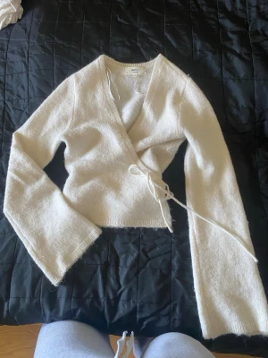 Vit omlottstickad tröja från Gina Tricot - Säljer en vit stickad omlott-tröja från Gina Tricot med långa ärmar och knytband i sidan. Tröjan har en mjuk och fluffig känsla, perfekt för lager-på-lager och en trendig look. Passar dig som gillar stilrena och enkla plagg.