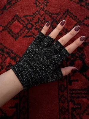 Svarta fingerlösa stickade vantar - Fingerlösa vantar i svart stickat material med diskret randigt mönster. Perfekta för dig som vill ha värme men ändå kunna använda mobilen eller skriva. Snyggt och enkelt designade, passar till många olika outfits.