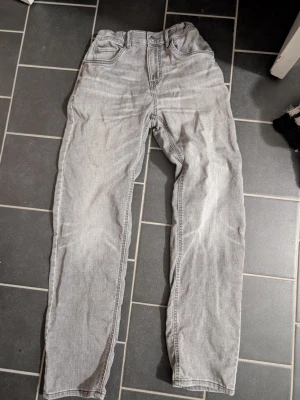 Ljusgrå raka jeans i bomull stl 164 - Säljer ett par ljusgrå jeans med rak passform och klassisk femficksdesign. Jeansen har bälteshällor och knappgylf. Tillverkade i bomull för en skön och avslappnad känsla. Perfekta till en casual look.