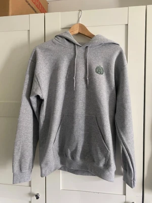Grå hoodie från Drakenberg - Oanvänd snygg grå hoodie från Drakenberg med grön patch på bröstet  och ett större tryck pp ryggen. Storlek S. Finns ett litet hål på sidan av ärmen, tröjan är använd en gång och kom med hålet på. Har en likadan oanvänd storlek M, utan hål som jag fick efter reklamation. Hör av dig vid frågor elr liknande!