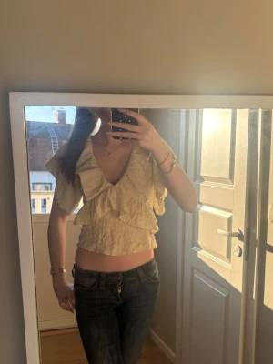 Beige croppad volangblus från Zara - Säljer en superfin beige croppad blus från Zara med volangdetaljer och v-ringning. Toppen har korta ärmar och är tillverkad i ett lätt, strukturerat material som känns luftigt och somrigt. Perfekt för dig som vill ha en trendig och söt topp till sommaren!