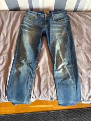 Blå jeans från Jack n Jones  - Säljer ett par klassiska blå jeans från Jack n Jones i storlek 33-34 med snyggt slitna detaljer och raka ben. Jeansen har fem fickor, gylf med dragkedja och är gjorda i mjuk denim. Det är en av de mer slim modeller av regular serien, perfekt för den som vill ha lite mer avslappnad stil men samtidigt trendig.