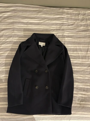 Marinblå dubbelknäppt kappa Vila - Stilren marinblå kappa från Vila i klassisk dubbelknäppt modell. Kappan har knappt används, så är i jätte fint skick. Finns inga defekter. (Finns hund i hemmet) så kan inte garantera att de inte kommer följa med nåt hundhår.                                                                                   