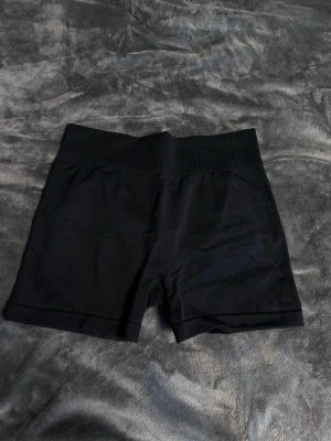 Svarta seamless cykelshorts - Säljer ett par svarta seamless cykelshorts med bred ribbad midjeresår och korta ben. Materialet är stretchigt och följsamt, perfekt för träning eller chill. Inga synliga loggor eller märken. Passar dig som gillar sportig och enkel stil.