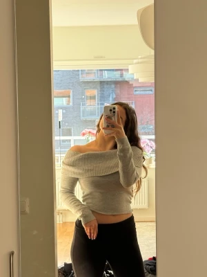 Grå croppad stickad tröja - Säljer en ljusgrå stickad tröja med bred ribbad krage som kan bäras både off-shoulder och uppvikt - justerbar krage! Tröjan är från Bershka och köpt för längesedan så kan faktiskt inte hitta original! - men aldrig använd utöver bilderna.