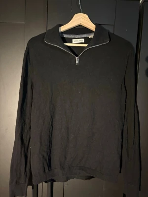 Svart halvzip-tröja Jack & Jones - Svart långärmad tröja från Jack & Jones med halv dragkedja och ståkrage. Tröjan har ribbade muddar vid ärmslut och nederkant, perfekt för en stilren och avslappnad look. Materialet är mjukt och bekvämt.