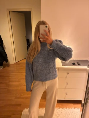 Ljusblå kabelstickad tröja - Mysig ljusblå kabelstickad tröja med rund hals och långa ärmar. Tröjan har en avslappnad passform och breda ribbade muddar vid ärmslut och nederkant. Perfekt för kalla dagar och enkel att styla till olika outfits.