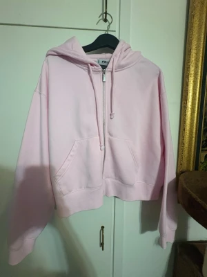 Ljusrosa cropped hoodie med dragkedja - Ljusrosa hoodie från H&M i cropped modell med dragkedja framtill och stor huva. Hoodien har känguruficka och ribbade muddar vid ärmslut och nederkant. Tillverkad i mjukt sweatshirtmaterial, perfekt för en chill och avslappnad stil.