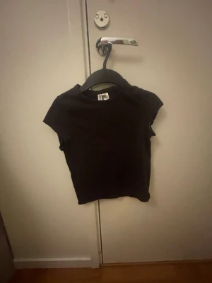 Bruncroppad t-shirt från H&M - En enkel och stilren brun  t-shirt från H&M med croppad passform och korta ärmar. Perfekt för att matcha med jeans eller kjol och passar dig som gillar en clean look.