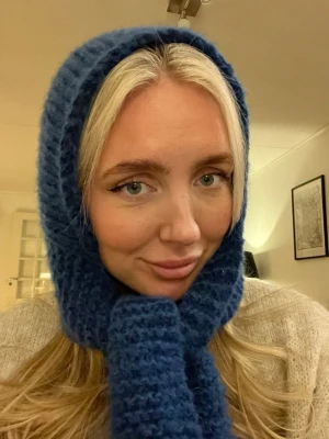 Blå stickad balaclava - Mysig blå handstickad balaclava med grov struktur och lång halsdel. Perfekt för kalla dagar och ger ett coolt, trendigt uttryck. Materialet är mjukt och värmande, ull alpacka mohair. Ingen synlig logga eller märke.