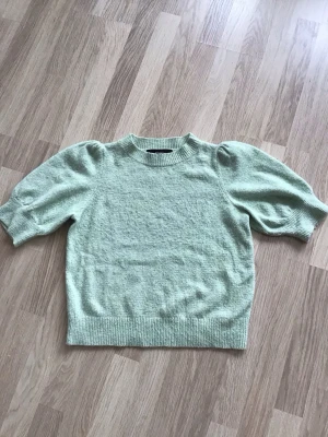 Ljusgrön stickad topp med puffärm från Vero Moda, stl S - Säljer en ljusgrön stickad topp med korta puffärmar från Vero Moda. Tröjan har ribbade muddar vid ärmslut och nederkant. Välanvänd, så ganska nopprig. Just nu fri frakt, så du betalar bara för toppen. Jag har fler plagg ute, och hittar du något mer från min garderobsutrensning, så skickar jag i samma paket.