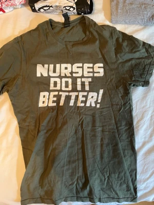 Grön t-shirt med tryck - Cool grön t-shirt med vit text 'NURSES DO IT BETTER!' på framsidan. Klassisk rund hals och korta ärmar, perfekt för dig som gillar statement-plagg. Materialet känns som bomull och passformen är normal.