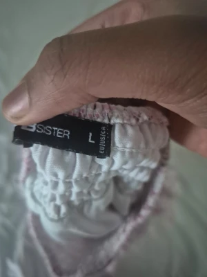 Vit och rosa kjol från FB Sister - Söt kort kjol från FB Sister i vitt med rosa detaljer. Kjolen har resår i midjan för en bekväm passform och är tillverkad i ett lätt material. Perfekt för dig som gillar en feminin och avslappnad stil.