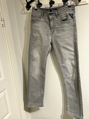 Grå raka jeans från Replay - Snygga grå jeans från Replay med raka ben. Jeansen har en diskret tvättad look och svarta detaljer vid fickan. Tillverkade i mjukt denimtyg som gör dom bekväma