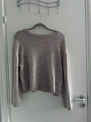 Ljusgrå stickad tröja med rund hals - Mysig ljusgrå stickad tröja med avslappnad passform och rundad halsringning. Tröjan har långa ärmar och ribbade muddar vid ärmslut och nederkant. Perfekt för lager på lager under kyliga dagar.