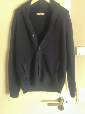 Mörkblå kofta med knappar - Mysig mörkblå kofta med tre knappar framtill och två fickor. Koftan har en avslappnad passform, lång ärm och bred krage. Perfekt att slänga över en t-shirt för en enkel men snygg look.